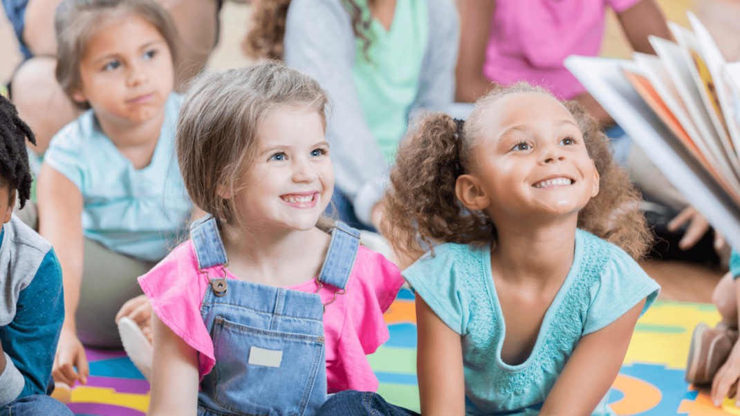 Two little girls smiling as someone reads a story to them.